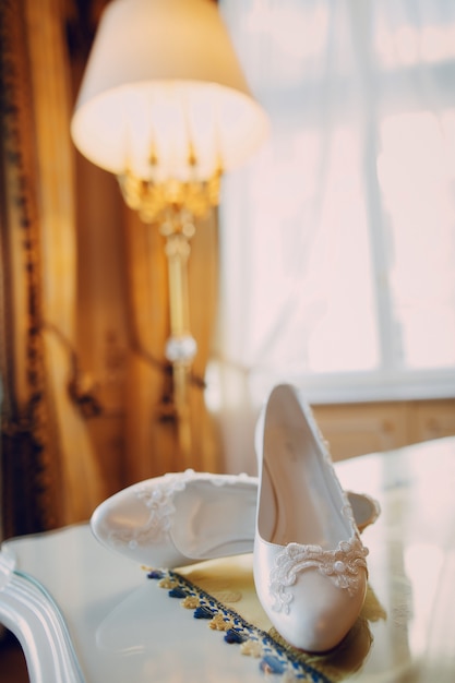 Hermosos zapatos blancos de novia de pie sobre la mesa en la habitación