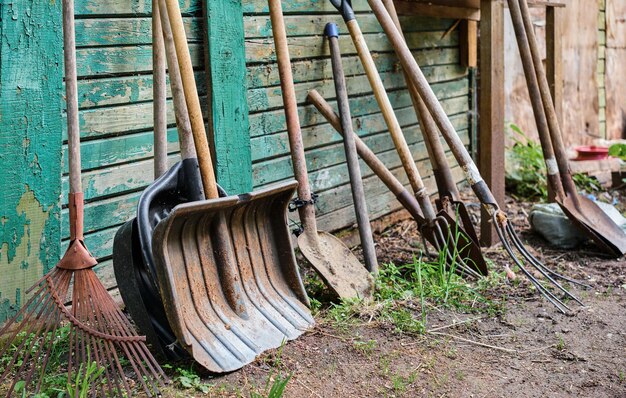 Herramientas antiguas de jardinería en una huerta de pared verde pelada de madera y equipo agrícola Enfoque selectivo trabajo manual de herramientas agrícolas en el suelo