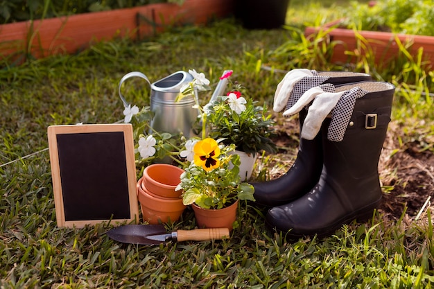 Herramientas de jardinería y flores en el suelo con pizarra en blanco