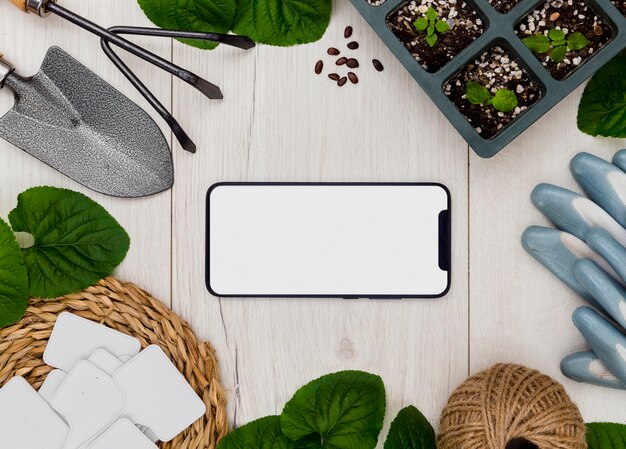 Herramientas de jardinería y plantas planas con teléfono en blanco