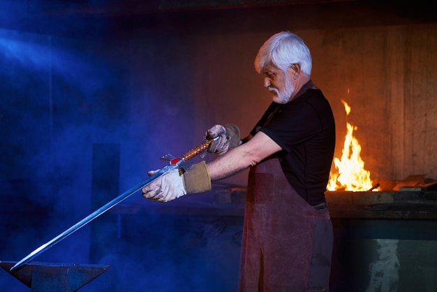 Foto gratuita herrero envejecido competente haciendo espada en la fragua