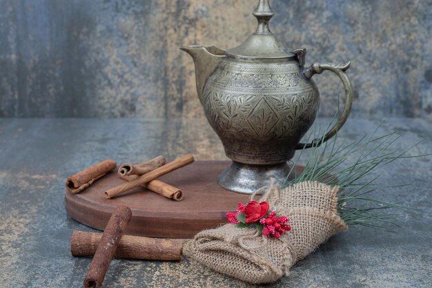 Hervidor antiguo con palitos de canela en placa de madera.