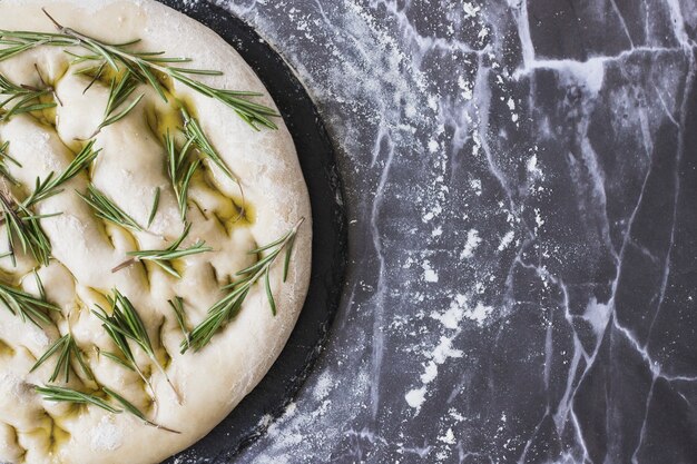 Hierbas de romero en masa de pan sin cocer en encimera de cocina