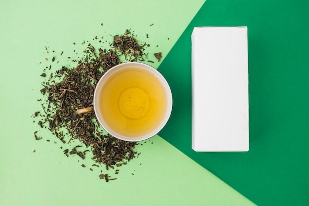 Foto gratuita hierbas con té verde y caja blanca sobre fondo verde