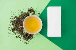 Foto gratuita hierbas con té verde y caja blanca sobre fondo verde