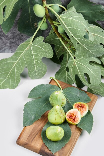 Higos con hojas verdes en una bandeja de madera.