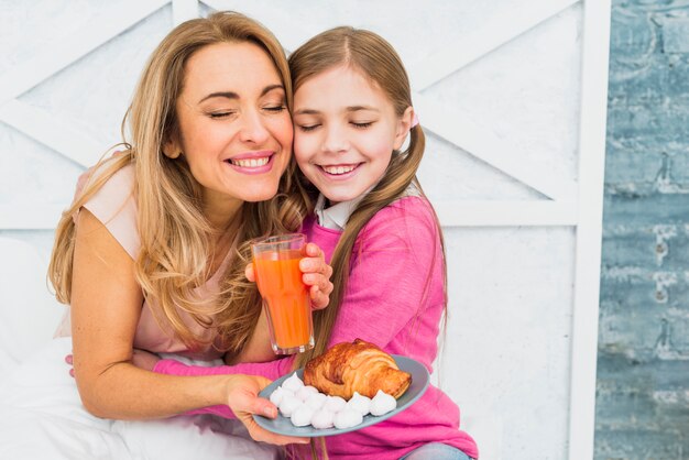 Hija abrazando a la madre con el desayuno en la cama