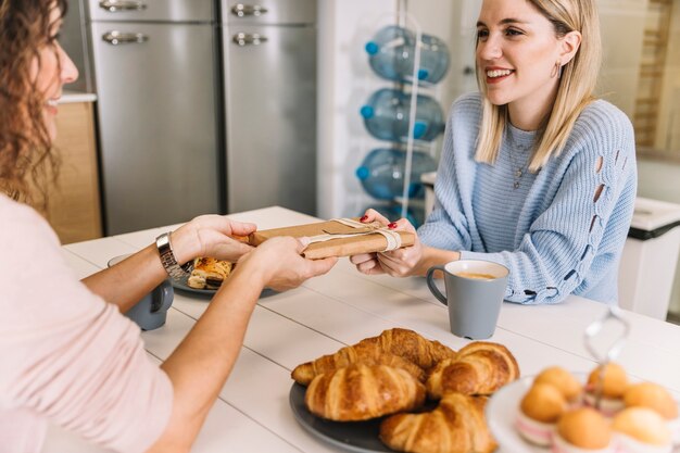 Hija alegre y madre con regalo durante el desayuno