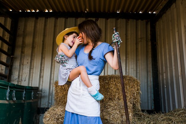 Hija de alimentación de manzana roja a su madre de pie delante de la pila de heno