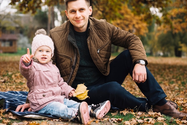 Foto gratuita hija apuntando lejos y sentado con papá en el parque de otoño