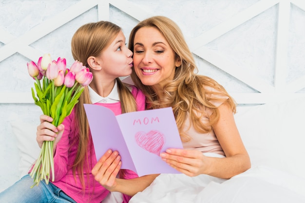 Hija besando a madre con tarjeta de felicitación