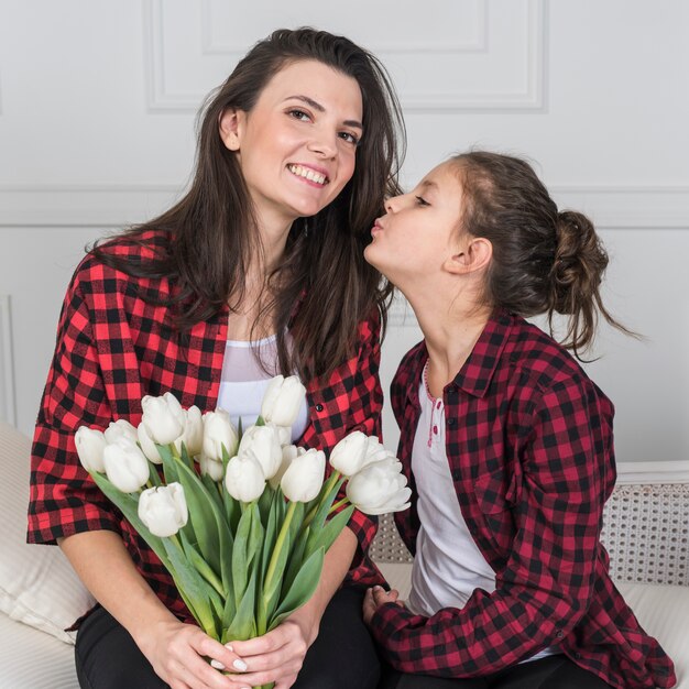 Hija besando a madre con tulipanes