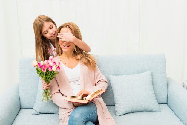 Hija cerrando los ojos a la madre y dando tulipanes.