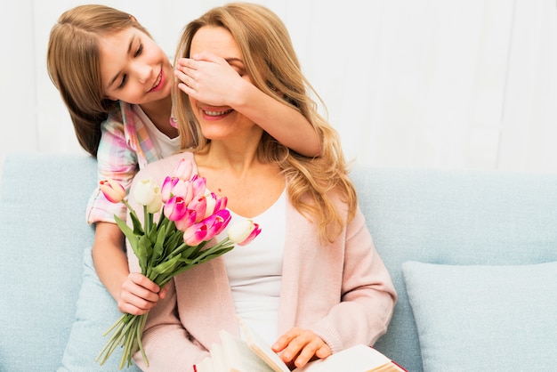Hija cerrando los ojos madre y regalando flores.