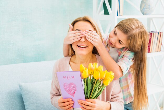 Hija cerrando ojos madre con regalos.