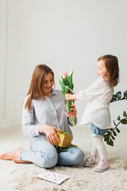 Hija dando flores a la madre con caja de regalo.