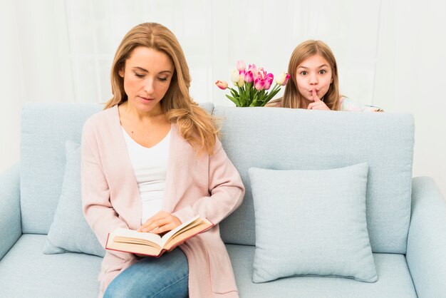 Hija escondida detrás del sofá con su madre
