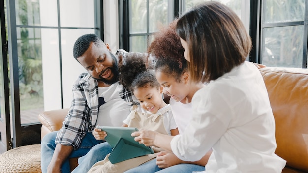 Hija y familia afroamericana joven feliz usando la tableta en casa.