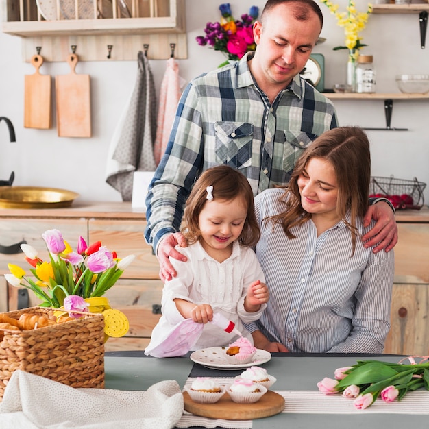 Hija feliz con padres haciendo cupcake en cocina