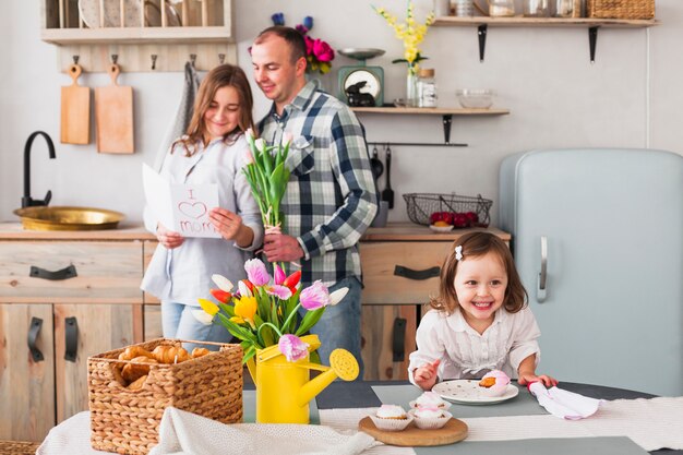 Hija feliz que hace la magdalena cerca de padres con la tarjeta de felicitación