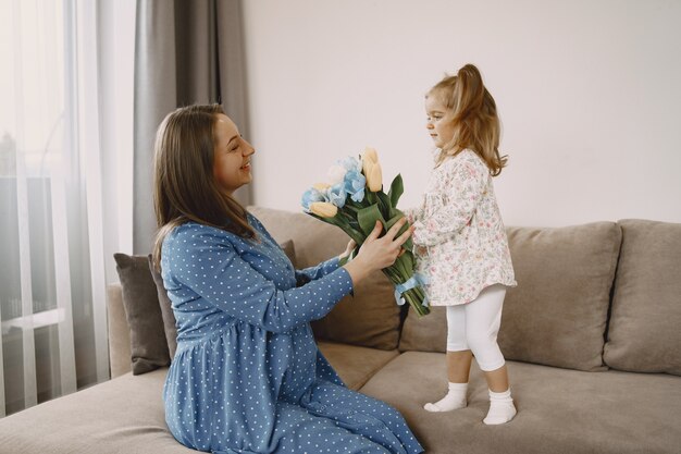 Hija con flores. Mamá embarazada en el sofá. Madre e hija con ropas brillantes.