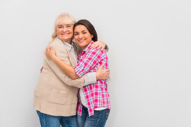 Hija joven sonriente que abraza a su madre mayor que se opone al fondo blanco