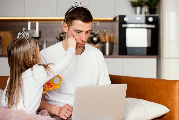 Hija jugando con el padre mientras trabaja en la computadora portátil