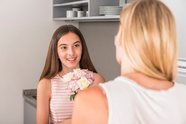 Hija linda que da flores a la madre en la cocina