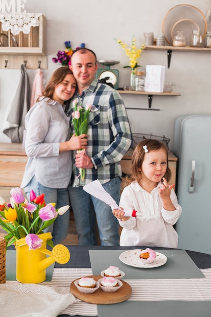 Hija linda que hace cupcake cerca de padres con flores