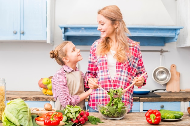 Hija mirando a su madre preparando la ensalada en la cocina