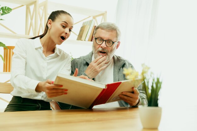 Una hija o nieta pasa tiempo con el abuelo o el hombre mayor. Día de la familia o del padre, emociones y felicidad. Retrato de estilo de vida en casa. Niña cuidando a papá. Leyendo un libro.