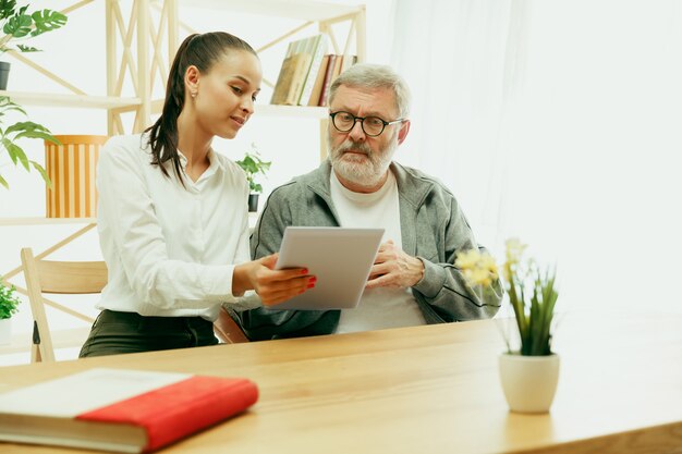 Una hija o nieta pasa tiempo con el abuelo o el hombre mayor. Día de la familia o del padre, emociones y felicidad. Retrato de estilo de vida en casa. Niña cuidando a papá. Usando una tableta.