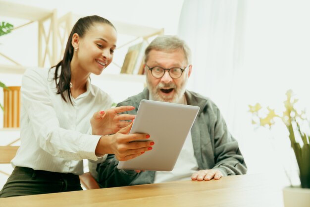 Una hija o nieta pasa tiempo con el abuelo o el hombre mayor. Día de la familia o del padre, emociones y felicidad. Retrato de estilo de vida en casa. Niña cuidando a papá. Usando una tableta.