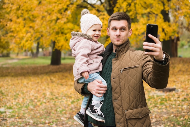 Hija de padre e hija haciendo selfie en otoño parque