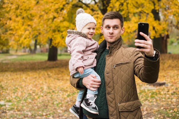 Hija de padre e hija haciendo selfie en otoño parque