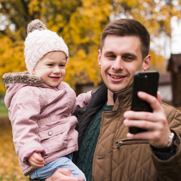 Hija y padre haciendo selfie en otoño parque