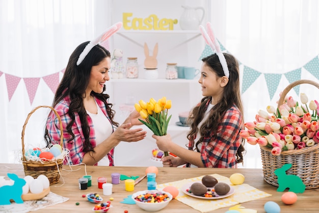 Hija que da tulipanes de flores amarillas a su madre con la preparación del día de Pascua en casa