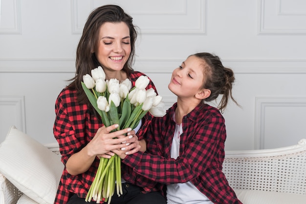 Foto gratuita hija que da tulipanes a la madre en el sofá