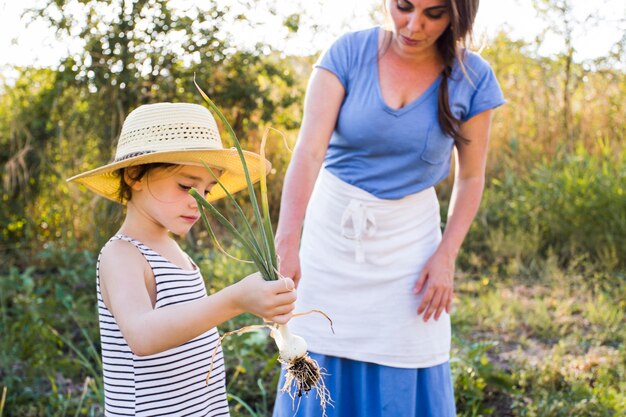 Hija que muestra a su madre la cebolla de primavera cosechada en el campo