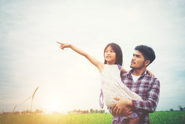 Hija señala lejos y que sonríe con su padre en los prados f