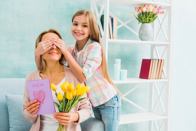 Hija sonriente y cerrando los ojos a la madre con regalos.