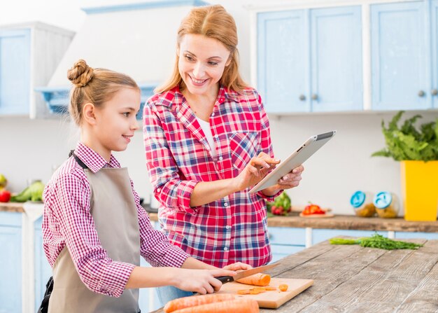 Hija sonriente que mira a su madre que muestra receta en el teléfono móvil