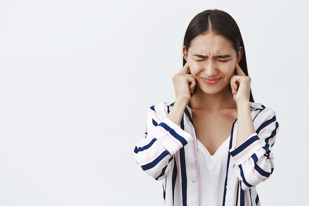 Hija tapándose los oídos disgustada por la fuerte pelea de los padres, sintiéndose intensa y tímida. Retrato de mujer linda infeliz y triste en blusa, frunciendo el ceño con los ojos cerrados tratando de no escuchar ruido