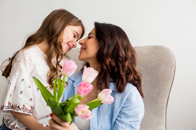 Hija con tulipanes abrazando a madre en sillón