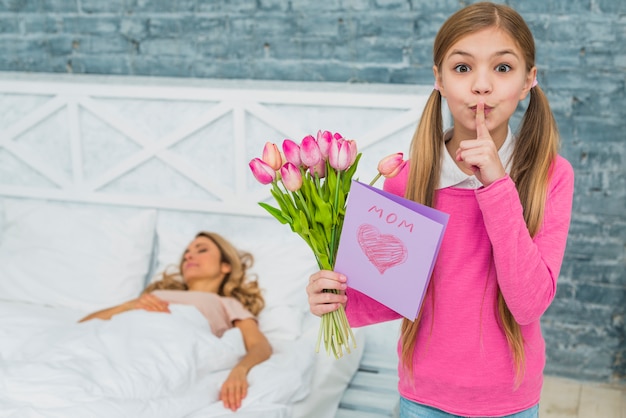 Hija con tulipanes y tarjeta de felicitación sosteniendo el dedo en los labios