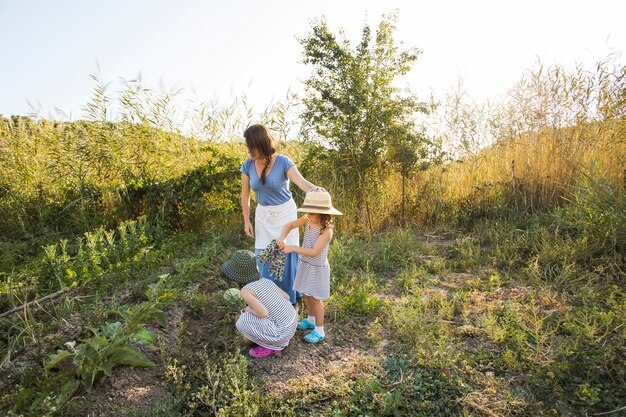 Hijas cosechando vegetales con su madre en el campo.