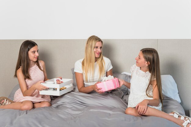 Hijas dando regalos a la madre en la cama.