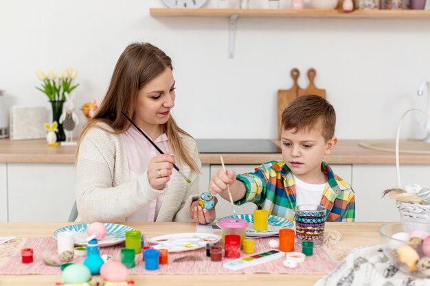 Hijo de alto ángulo ayudando a mamá a pintar huevos