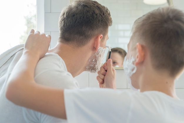 Foto gratuita hijo ayudando a su padre a afeitarse desde atrás