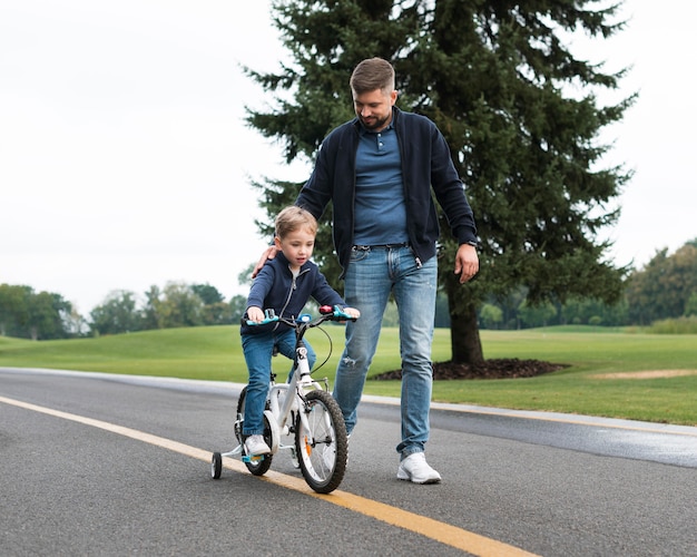 Hijo en bicicleta en el parque junto a su padre.